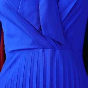 Detailed view of bright blue pleated dress featuring a V-neckline and textured twill fabric