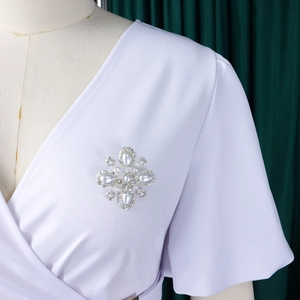 Detailansicht einer silbernen Kreuzbrosche mit Perlen und Strasssteinen auf V-Ausschnitt Kleid