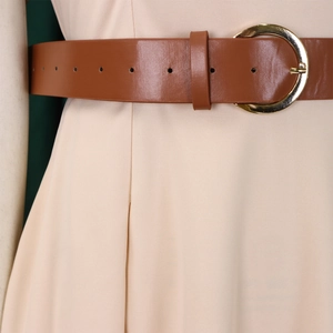 Close-up of a brown faux leather belt with a round gold buckle on a light beige dress
