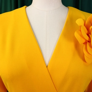 Close-up of elegant yellow V-neck dress featuring a large 3D floral accent on shoulder