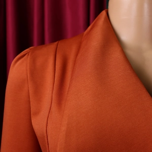 Detailed close-up of the notched lapel and pleated shoulder on an orange dress