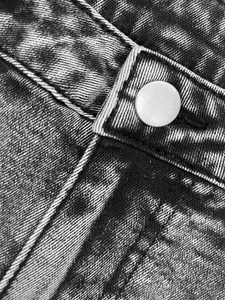 Detail of snow wash denim fabric with silver metal button and contrast double stitching
