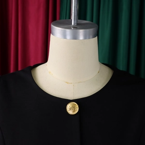 Detail of elegant black crew neck jacket featuring a textured gold embossed button