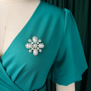 Detail einer Blumenbrosche mit ovalen Perlen und Straßsteinen auf V-Ausschnitt Kleid