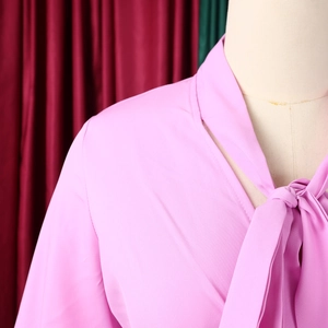 Detail of pink satin V-neck shirt with elegant tie-bow and smooth pleated fabric texture