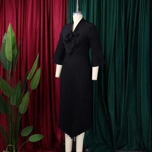 Detail of elegant black pleated midi dress featuring V-neckline with a large bow tie