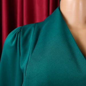 Detail of dark green dress showing twill fabric texture, pleated puff sleeves and V-neckline
