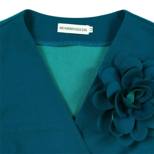 Detailed view of the teal V-neck dress featuring a large 3D fabric flower and brand label
