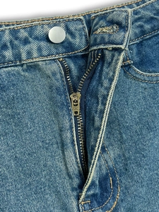 Detail view of denim skirt pants showing waist button, metal zipper, and washed blue fabric