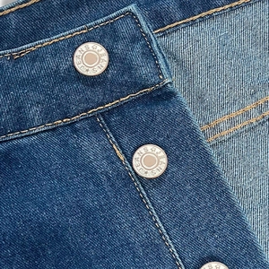 Detail of silver metal button with JEANS text and yellow double stitching on denim jeans
