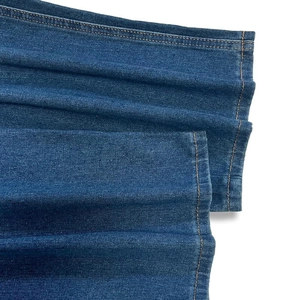 Detailed close-up showing the dark blue denim fabric texture and orange double-stitched hem