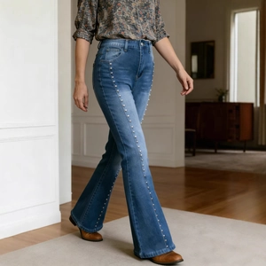 Detail of high-waist flared jeans featuring silver metal rivets on side seams and blue wash