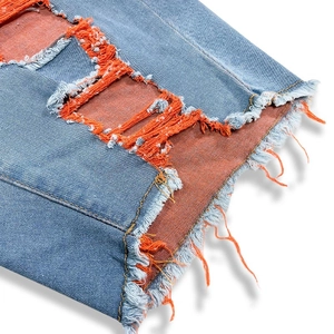 Detail aus hellblauem Denim mit Distressed-Löchern und orangefarbenem Netzfutter