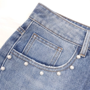 Dettaglio delle perle e dei rivetti metallici sulle tasche dei jeans in denim azzurro