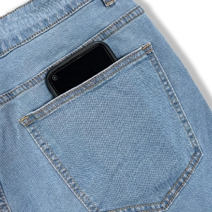 Detailansicht der großen Gesäßtasche an hellblauer Jeans mit einem schwarzen Smartphone