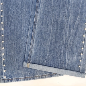 Dettaglio di perle su jeans in denim lavaggio sfumato azzurro con orlo ripiegato