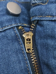 Detailed close-up of durable SBS metal zipper and button on blue flare jeans