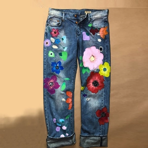 Detail of blue straight jeans featuring colorful floral hand-painted art and cuffed hems