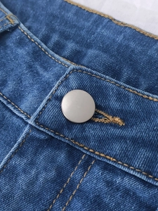 Detailed macro view of dark indigo denim waist with metal button and orange stitching