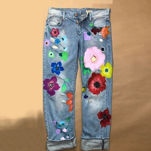 Detail of light blue straight jeans with colorful floral print and distressed elements