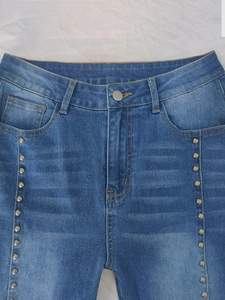 Detail of silver rivets on high-waisted blue jeans with orange contrast stitching