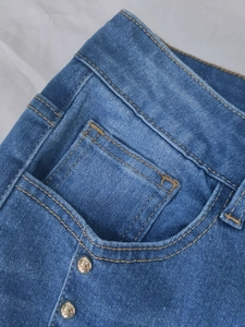 Detail of high waist flare jeans showing orange stitching and silver rivets on the pocket