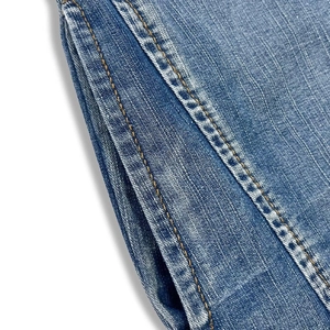 Close-up of light blue denim fabric texture with orange double stitching on pocket