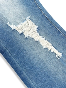 Détail du design déchiré avec fibres effilochées sur le jean skinny bleu délavé