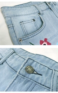 Close-up of floral embroidery and metallic rivets on light blue denim jeans waist