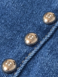 Detailed close-up of polished silver rivets and stitching on dark blue denim fabric