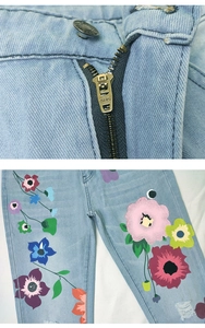 Detail of blue straight jeans featuring floral print, SBS zipper, and ripped hems