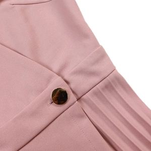 Detail of pink dress featuring a polished gold button and fine pleated fabric textures