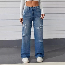 Detail of high-waisted distressed wide-leg jeans with ripped knees and whiskers