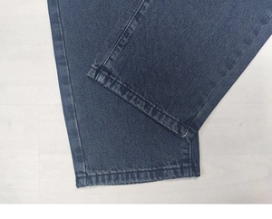Detailed close-up showing the reinforced double-stitch hem on dark blue denim pants