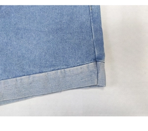 Detailed macro view of folded hem stitching on light blue denim shorts for summer