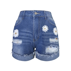 Detail of high-waisted blue denim shorts featuring white daisy embroidery and floral patches
