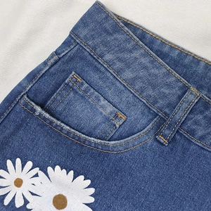 Close-up of dark blue denim shorts featuring orange stitching and white daisy prints