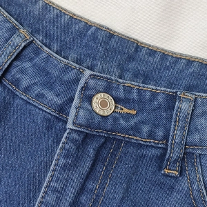 Close-up of blue denim jeans featuring twill texture and branded metal button