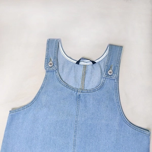 Close-up detail of light blue denim pinafore dress with metal buckles and U-neckline