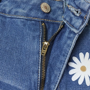 Detailed close-up of blue denim shorts with metal zipper, button and daisy flower print