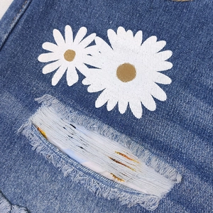 Macro detail of blue denim shorts featuring white daisy print and distressed frayed hems