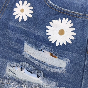 Women's blue denim shorts featuring white daisy floral print and distressed frayed hems