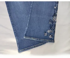 Detail shot of white floral embroidery on the hem of blue flared high waist denim jeans