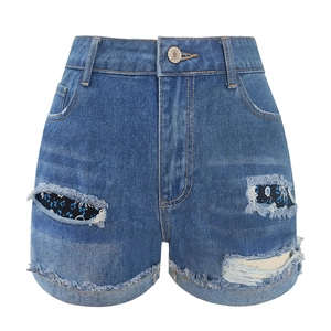 Close-up of high-waist distressed denim shorts with floral patches and frayed hems