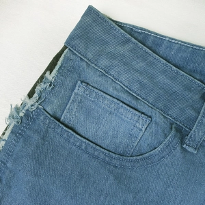 Detailed macro view of denim jeans featuring raw fringe edges and precision stitching