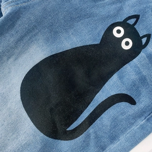 Détail d'un jean bleu avec un grand imprimé de chat noir en dessin animé sur le tissu