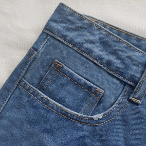 Detailed macro view of the waist structure and yellow contrast stitching on denim shorts