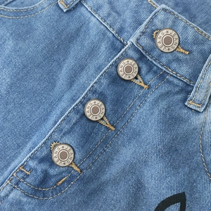 Détail des boutons en métal vintage et coutures orange sur un jean en denim bleu foncé