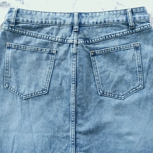 Detail of light wash denim skirt back pockets and belt loops with clean stitching