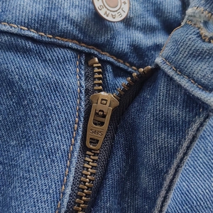 Close-up of metal zipper with SBS logo and JEANS button on blue denim shorts